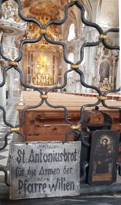 Bild, welches einen Einblick in Basilika von Wilten (Innsbruck) gibt; und ein Schild zeigt, welches um Antonius-Brot für arme Menschen aus der Pfarrei bittet.